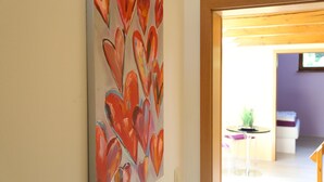 A room with a large abstract painting on the wall, a small round table with a plant, and a bed in the background. - Ferienwohnung in Freital, Dresden (Freital)
