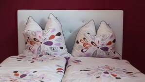 A bed with a white headboard and two decorative pillows with floral patterns. - Ferienwohnung in Freital, Dresden (Freital)