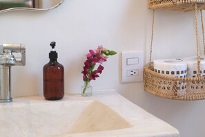 A bathroom sink with a soap dispenser, a vase with flowers, and a hanging basket with toiletries.