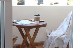 A small wooden table with a coffee cup, a newspaper, and a chair with a white cloth.