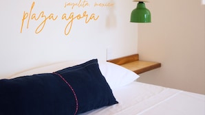 Un dormitorio con una cama, un almohadón, una mesita de noche y una lámpara verde de pared.