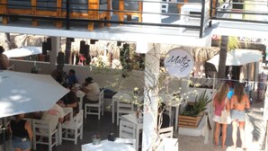 Un área de estar al aire libre con mesas y sillas blancas, un letrero colgante que dice 'Matz' y vista a la calle.