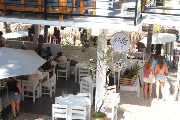 An outdoor seating area with white tables and chairs, a hanging sign for 'Matz', and a view of the street.