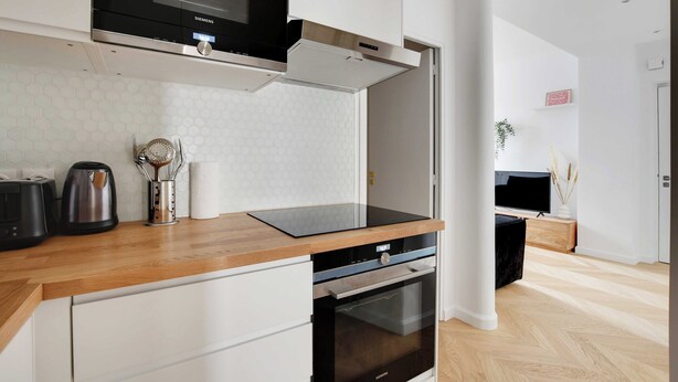 A modern kitchen with white cabinetry, a black microwave, and a stainless steel oven. - Spacious Cosy Apartment -2br/8p- Pl. de la Nation (Paris)