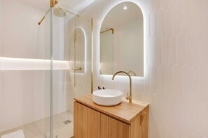 Ein modernes Badezimmer mit einer gläsernen Dusche, einem Holzlagerfläschchen und einem großen Spiegel.