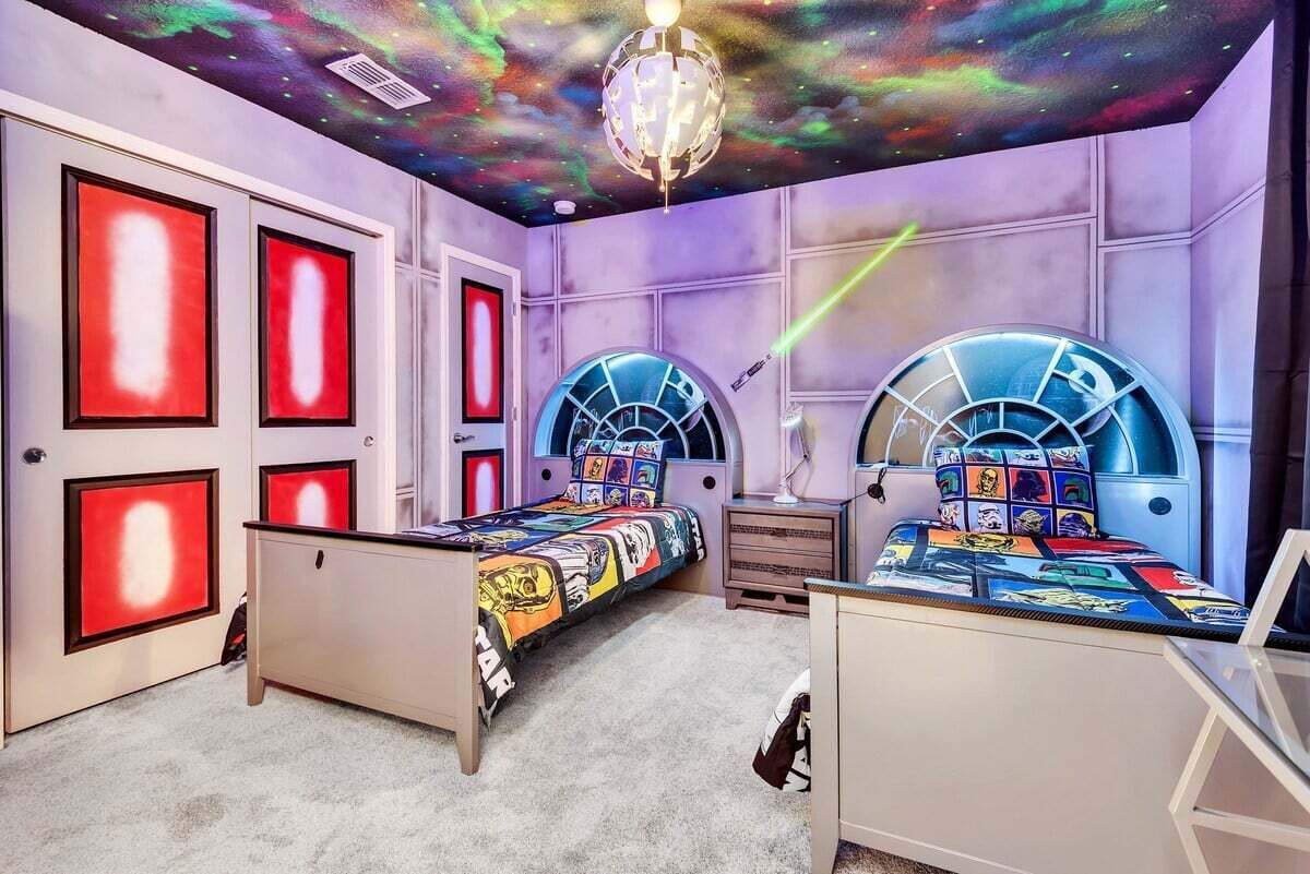 A bedroom with two beds, each with a unique design, a galaxy-themed ceiling, and a starry night design on the walls.