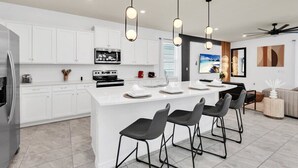 A modern kitchen with white cabinetry, a central island with bar stools, pendant lighting, and a large window.