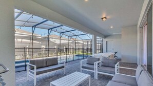 An outdoor patio with a pool, white furniture, and a glass enclosure.