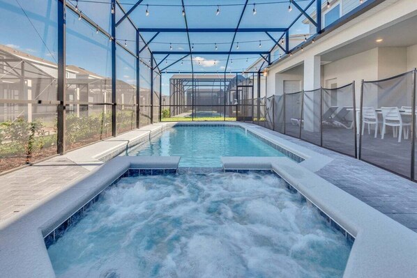 A hot tub area with a glass enclosure, surrounded by lounge chairs and a pool.