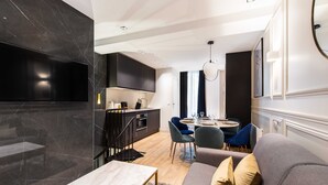A modern living room with a grey sofa, a small table, and a kitchen area with dark cabinetry and a marble backsplash. - Cosy Apart - 3br/6p - Jardin du Luxembourg/odeon (Paris)