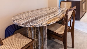 A dining area with a marble table, wooden chairs, a blue abstract painting, and a kitchen in the background. - Gorgeous Apartment - 2br/8p - Le Marais (Paris)