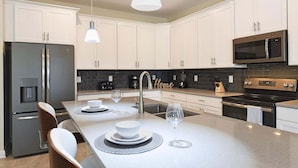 Una cocina moderna con armarios blancos, electrodomésticos de acero inoxidable y una isla central con asientos.