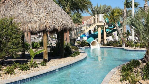 Un área de piscina con una estructura de techo de paja, palmeras y un tobogán.