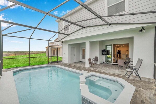 Piscina com hidromassagem, área de estar externa e um pátio coberto com vista para a paisagem ao redor.