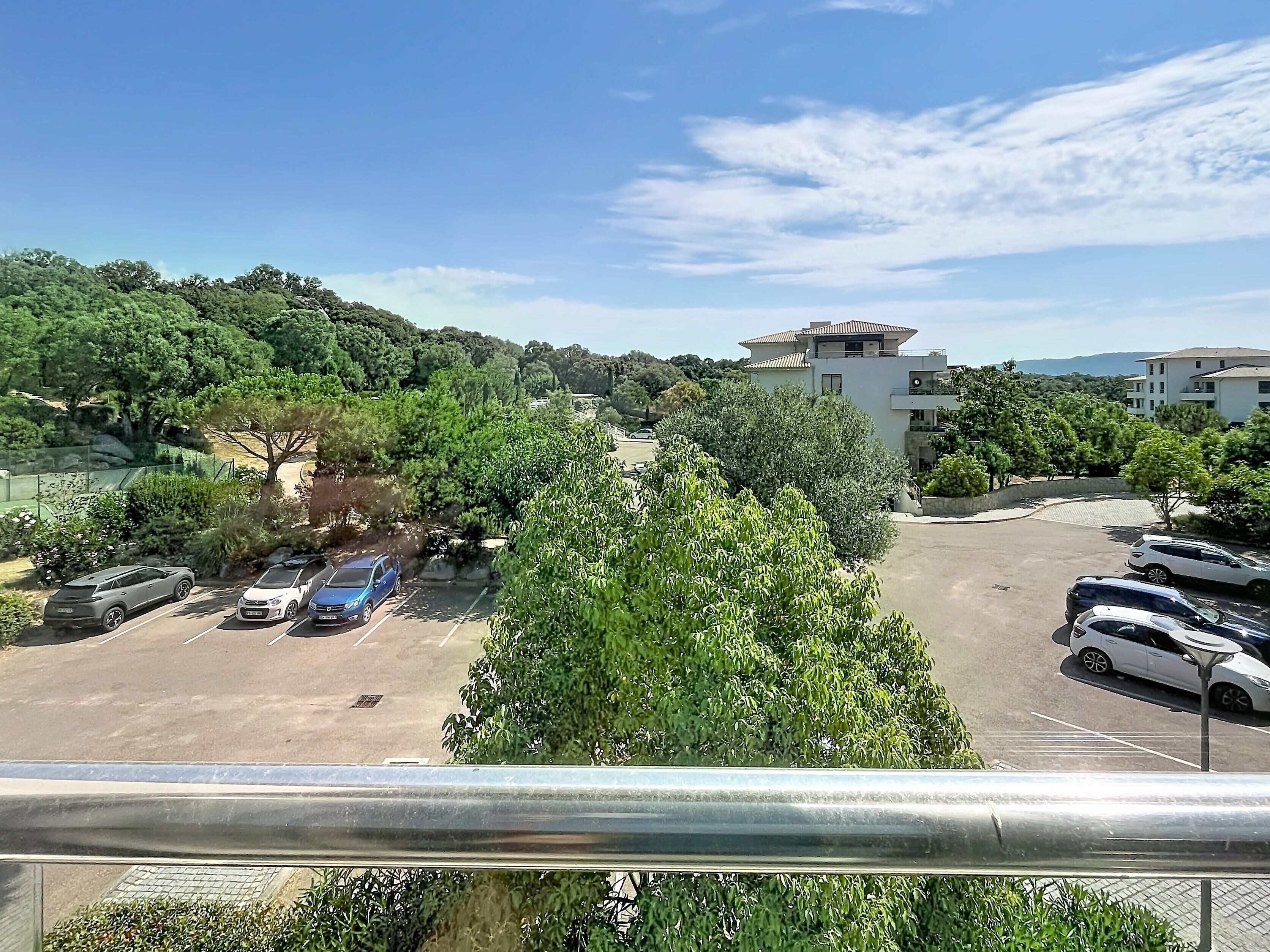 A parking lot with several cars, surrounded by greenery and buildings.