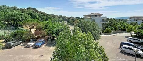 A parking lot with several cars, surrounded by greenery and buildings.