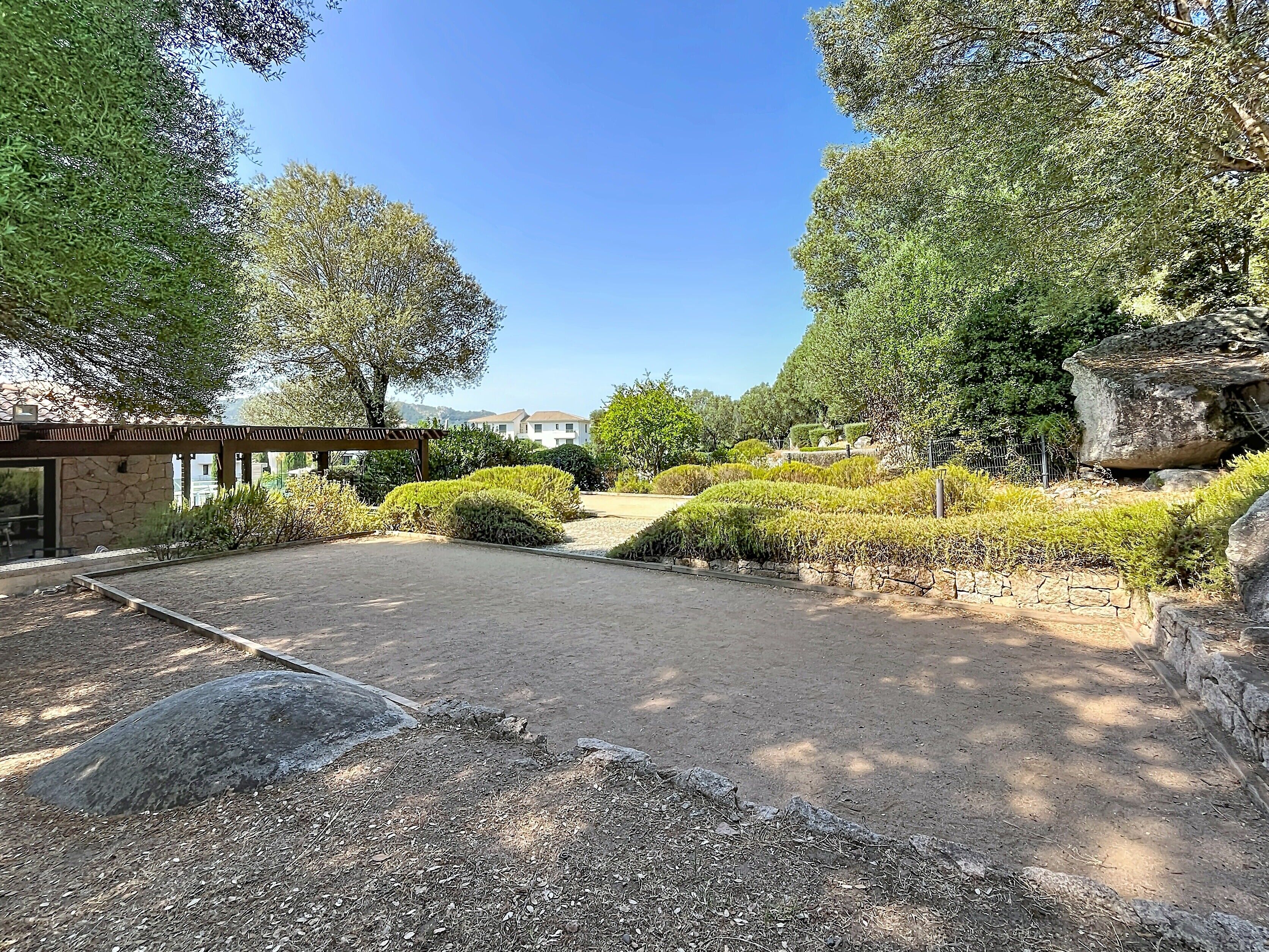 Un jardin agrémenté d’une pergola, de murs en pierre et d’un ciel dégagé.