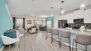A modern kitchen with white cabinets, a black refrigerator, a microwave, and a coffee maker. There are two bar stools and a dining table with chairs.