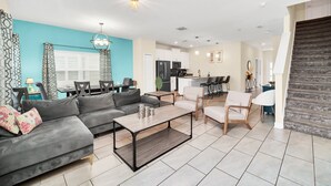 A modern living room with a sofa, coffee table, and chairs. There is a kitchen area with appliances and a dining table.