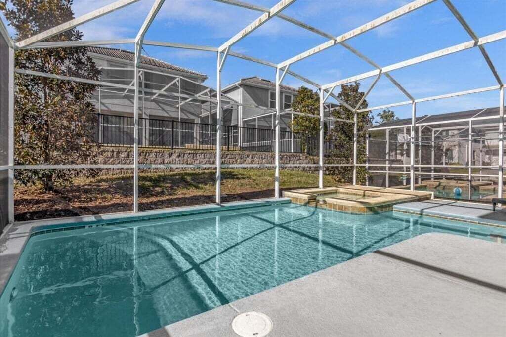 Ein Schwimmbecken mit Glasveranda, umgeben von einer Steindeck und Blick auf Wohnhäuser.