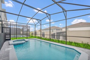 Ein Schwimmbad mit Glasveranda, umgeben von einem angelegten Garten und Wohngebäuden.