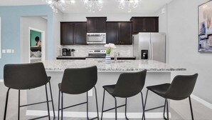 A modern kitchen with dark cabinets, a large island with bar stools, stainless steel appliances, and a unique chandelier. - Last Minute Disney! Private Pool, Hot Tub, Game Room & Themed Bedrooms. Book Now! #WIR405 (Orlando)