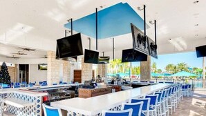 A modern bar area with a long counter, blue chairs, and multiple TVs mounted on the ceiling. - Last Minute Disney! Private Pool, Hot Tub, Game Room & Themed Bedrooms. Book Now! #WIR405 (Orlando)