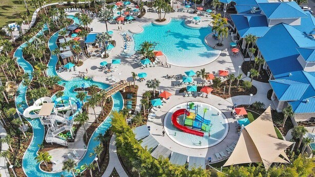 An aerial view of a resort with a large central pool, multiple water slides, and sun loungers.