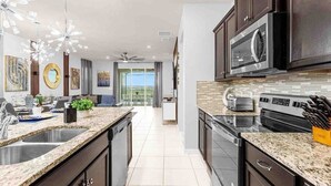 A modern kitchen with dark cabinetry, granite countertops, stainless steel appliances, and pendant lighting.