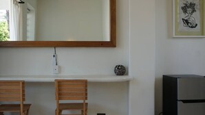 Een keuken met een houten aanrecht, twee houten stoelen, een koelkast, een spiegel aan de muur, en een klein decoratief object op de plank.
