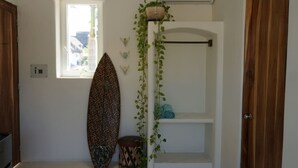 Een kamer met een surfplank, een raam, een plank met handdoeken en een airconditioner.