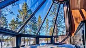 Acogedora habitación de cabaña con una cama grande, paredes de madera y vistas a un bosque nevado a través de amplios ventanales.