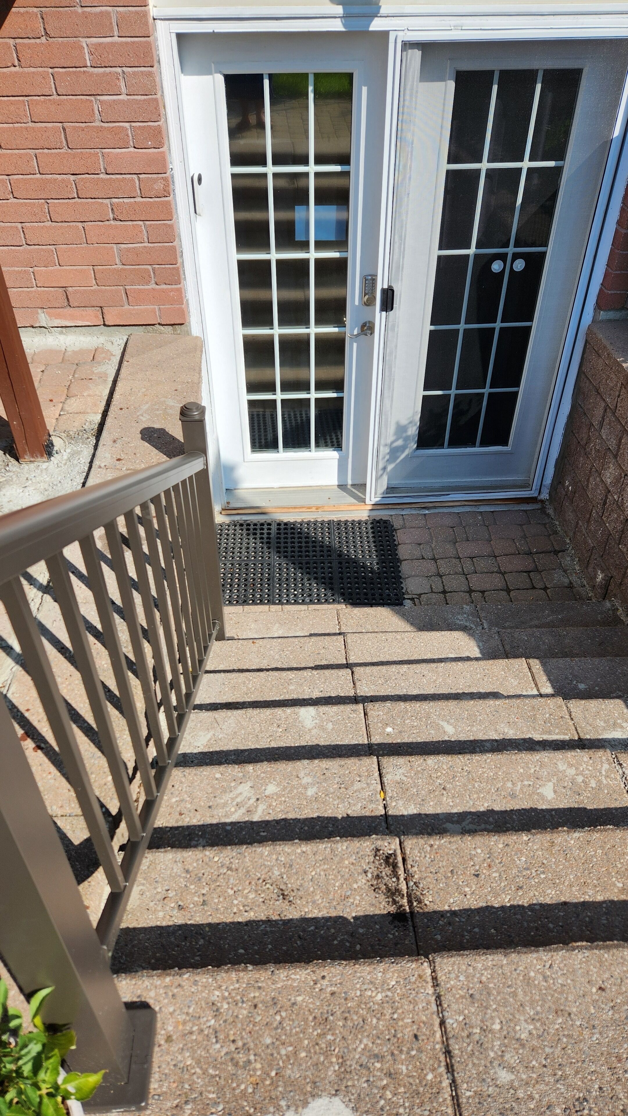 A set of outdoor stairs leading to a white door with a keypad lock, a metal handrail, and a small mat at the bottom.