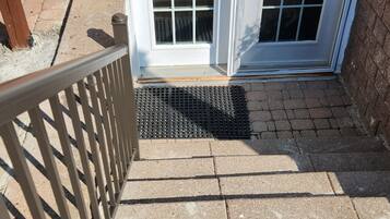 A set of outdoor stairs leading to a white door with a keypad lock, a metal handrail, and a small mat at the bottom.