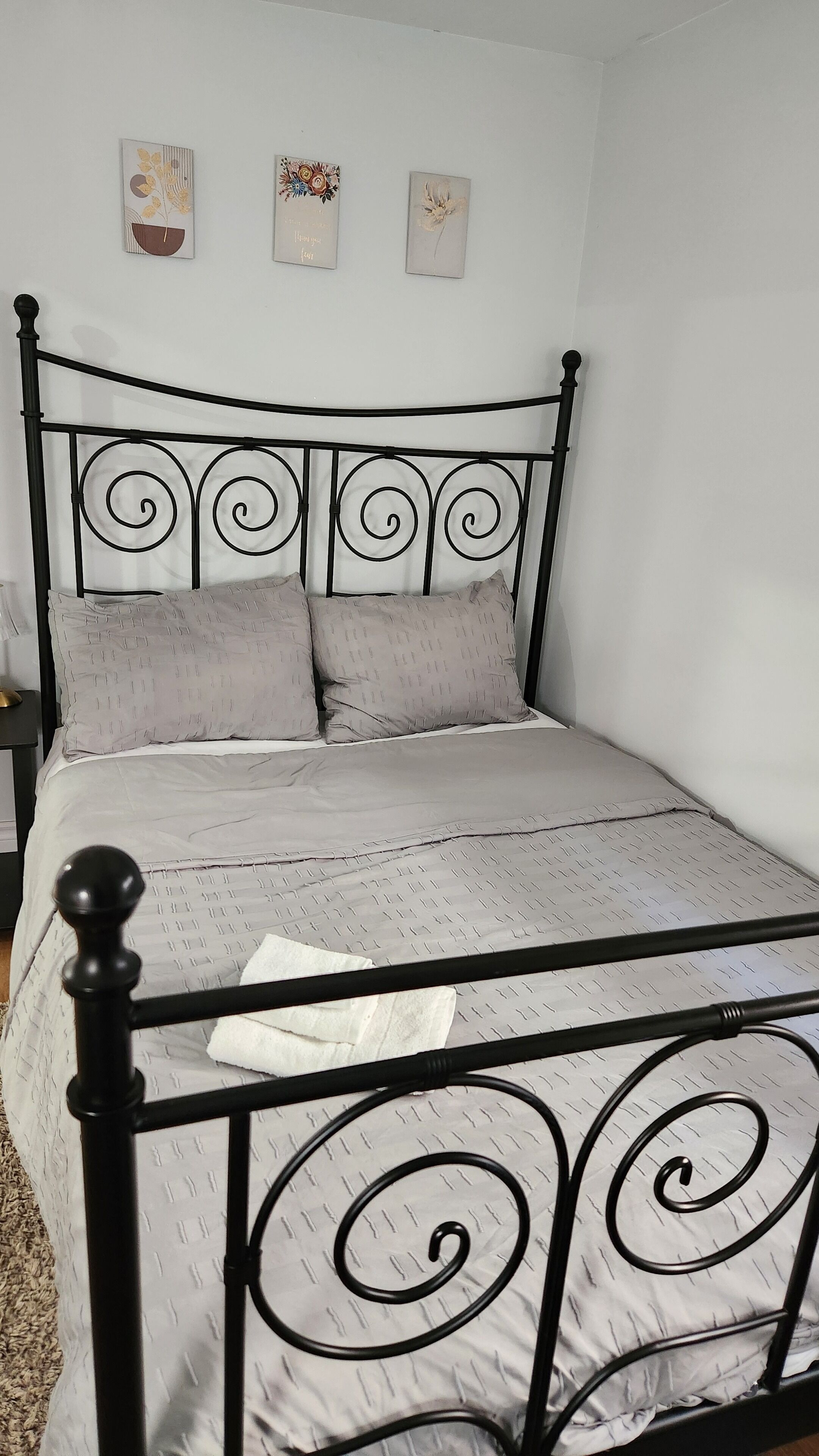 Un lit avec un cadre en métal, une literie grise et deux œuvres d’art accrochées au mur.