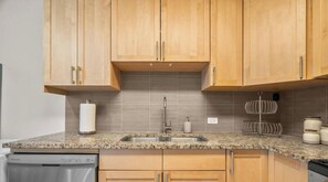 Una cocina con armarios de madera, encimera de granito, pileta de acero inoxidable y escurreplatos.