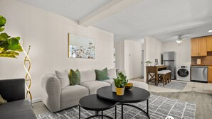 A modern living room with a sofa, coffee table, and a painting on the wall. - Steps to 17 Ave, 2 queens, UG parking, AC (Calgary)