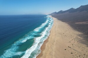 A coastal landscape with a beach, ocean, and mountains.