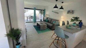 A modern living room with a sofa, coffee table, and dining area with chairs. - MarVillaFuerte - One Bedroom Apartment, Sleeps 4 (La Oliva)