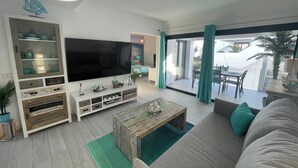 A modern living room with a large flat-screen TV, a wooden coffee table, and a sofa with green cushions. - MarVillaFuerte - One Bedroom Apartment, Sleeps 4 (La Oliva)