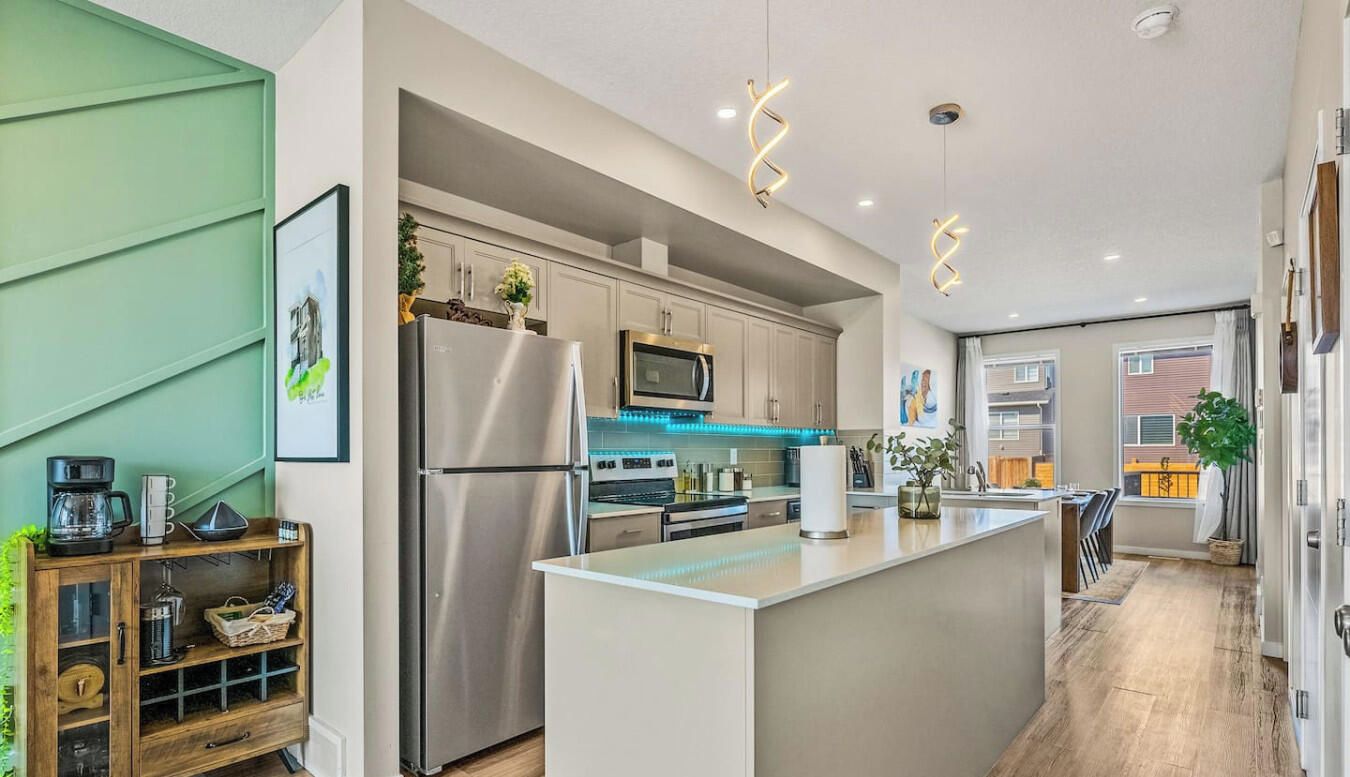 A modern kitchen with stainless steel appliances, a central island, and a green accent wall.