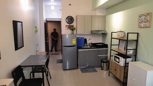 Cocina compacta con refrigerador, estufa, microondas y un pequeño comedor con mesa y sillas.