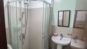 Un baño con ducha envuelta en vidrio, un lavamanos y un espejo.