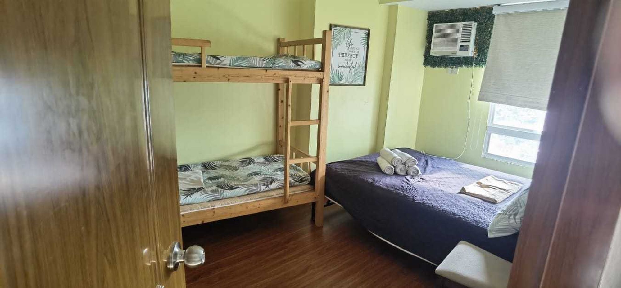 Un dormitorio con literas, una ventana con persianas, un equipo de aire acondicionado y una cita enmarcada en la pared.