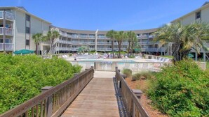 A resort with a pool area, multiple balconies, and a wooden boardwalk leading to the pool.