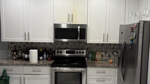 A modern kitchen with white cabinets, a stainless steel microwave, oven, and refrigerator. - 4-bedroom 3 bathroom room house with AC with Private Pool in great Pompano Beach (Pompano Beach)