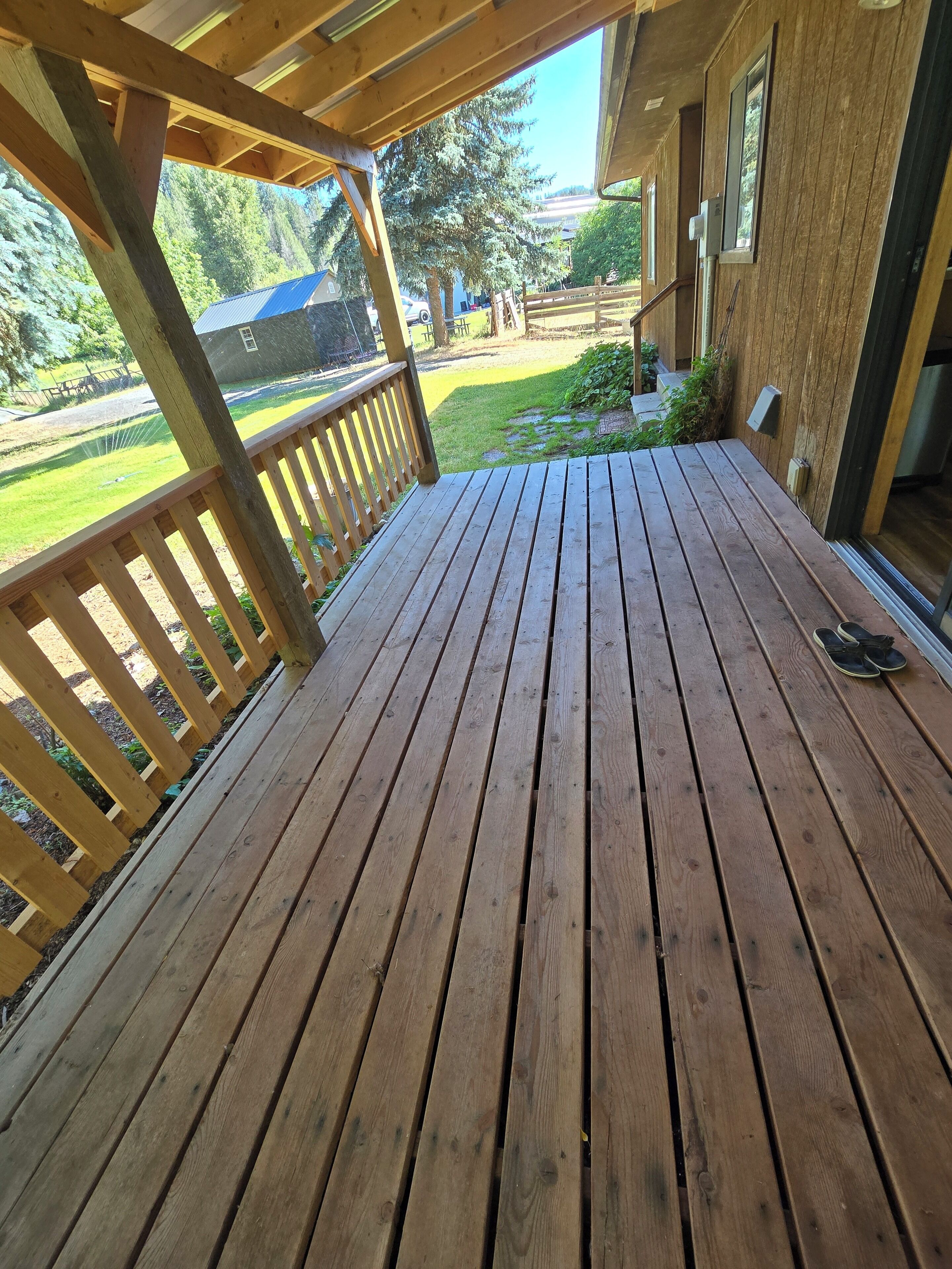 A wooden deck with a railing, overlooking a grassy yard and a house.