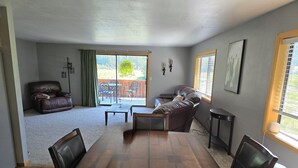 A spacious living room with a large wooden dining table, leather sofas, and a sliding glass door leading to a patio. - Country Living 6 miles from Colville, easy access, on a beautiful large pond! (Colville)