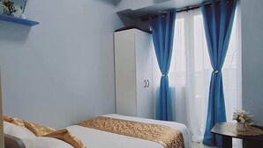 A bedroom with a bed, a desk, an air conditioning unit, and a window with curtains.