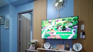 A living room with a flat-screen TV mounted on the wall, a wooden entertainment unit below, and a patterned rug on the floor.